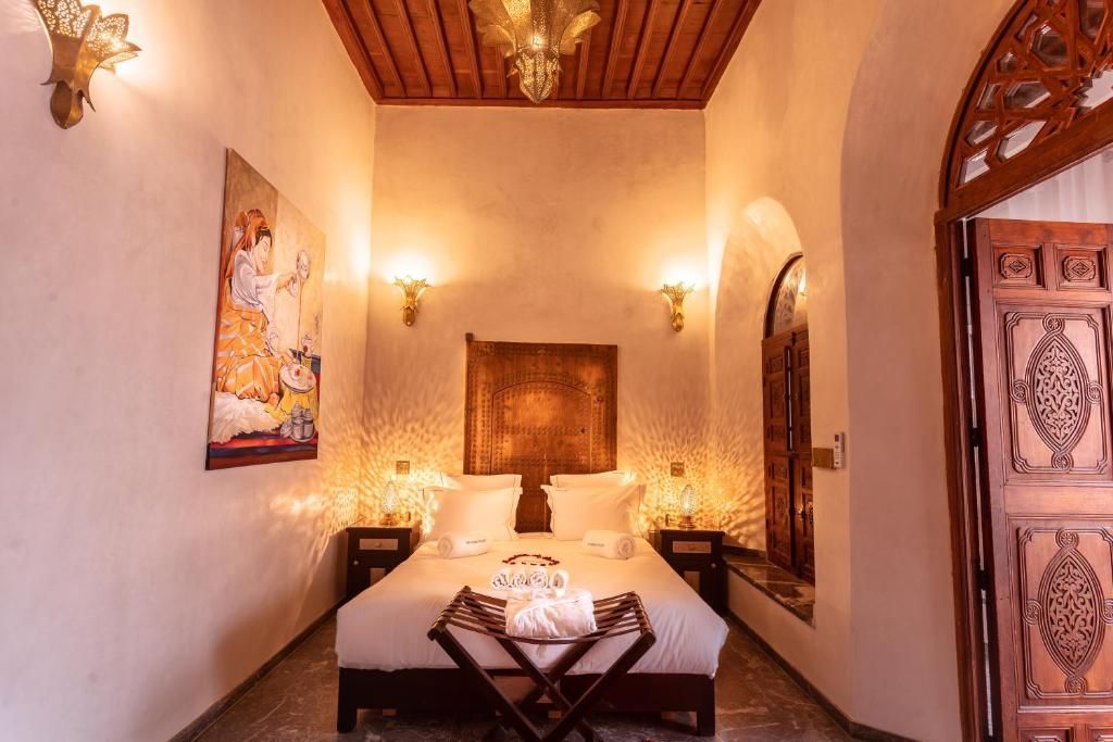 Bedroom with a bed, artwork, and carved wooden door. Warm lighting and ornate ceiling details.