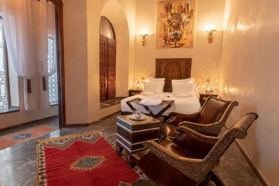 Cozy bedroom with red rug, leather chairs, double bed, and carved wooden door.