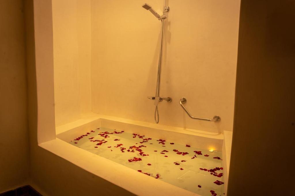 Bathtub filled with water and rose petals, built into a recessed wall. Showerhead and grab bar visible.