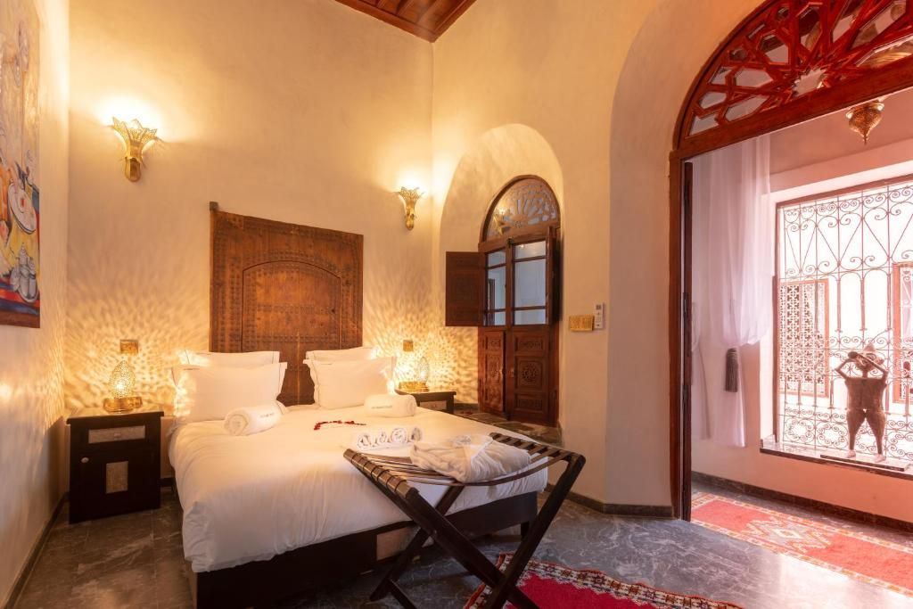 Bedroom with a double bed, ornate wooden headboard, and doorway leading to a courtyard.