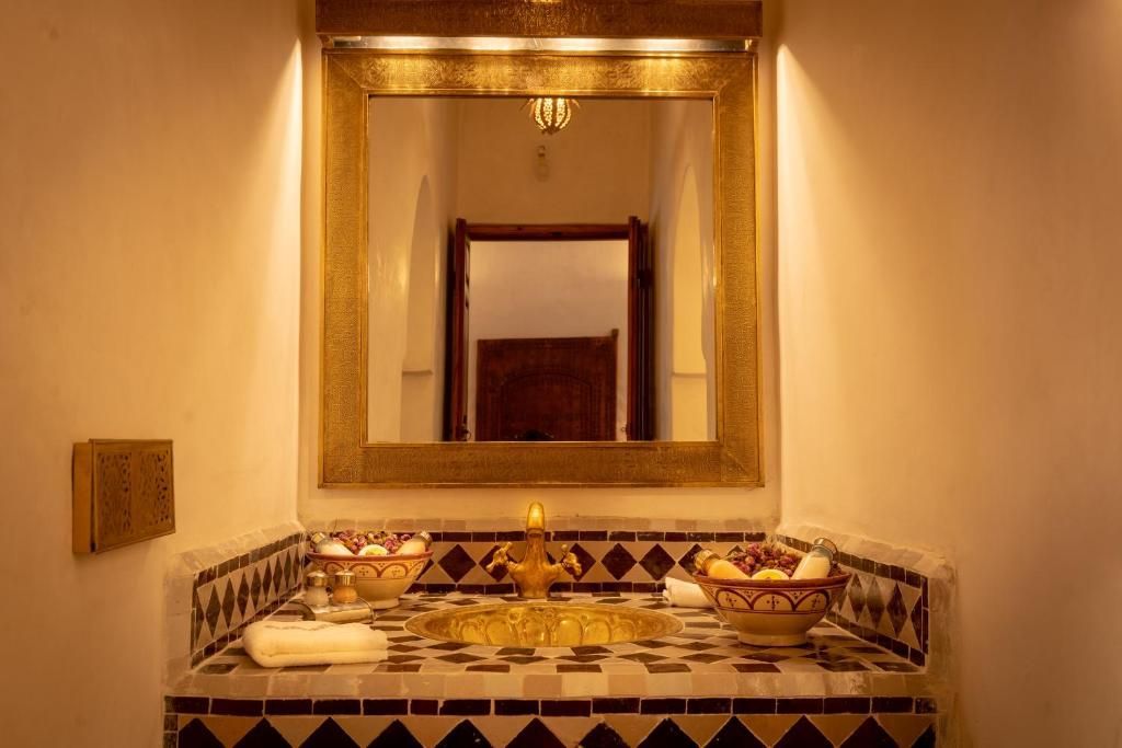 Bathroom with gold-framed mirror, ornate tiled counter, gold sink, and warm lighting.