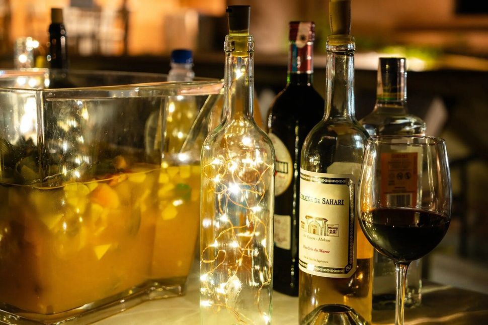 Wine bottles with fairy lights, a punch bowl, and a glass of red wine on a counter.