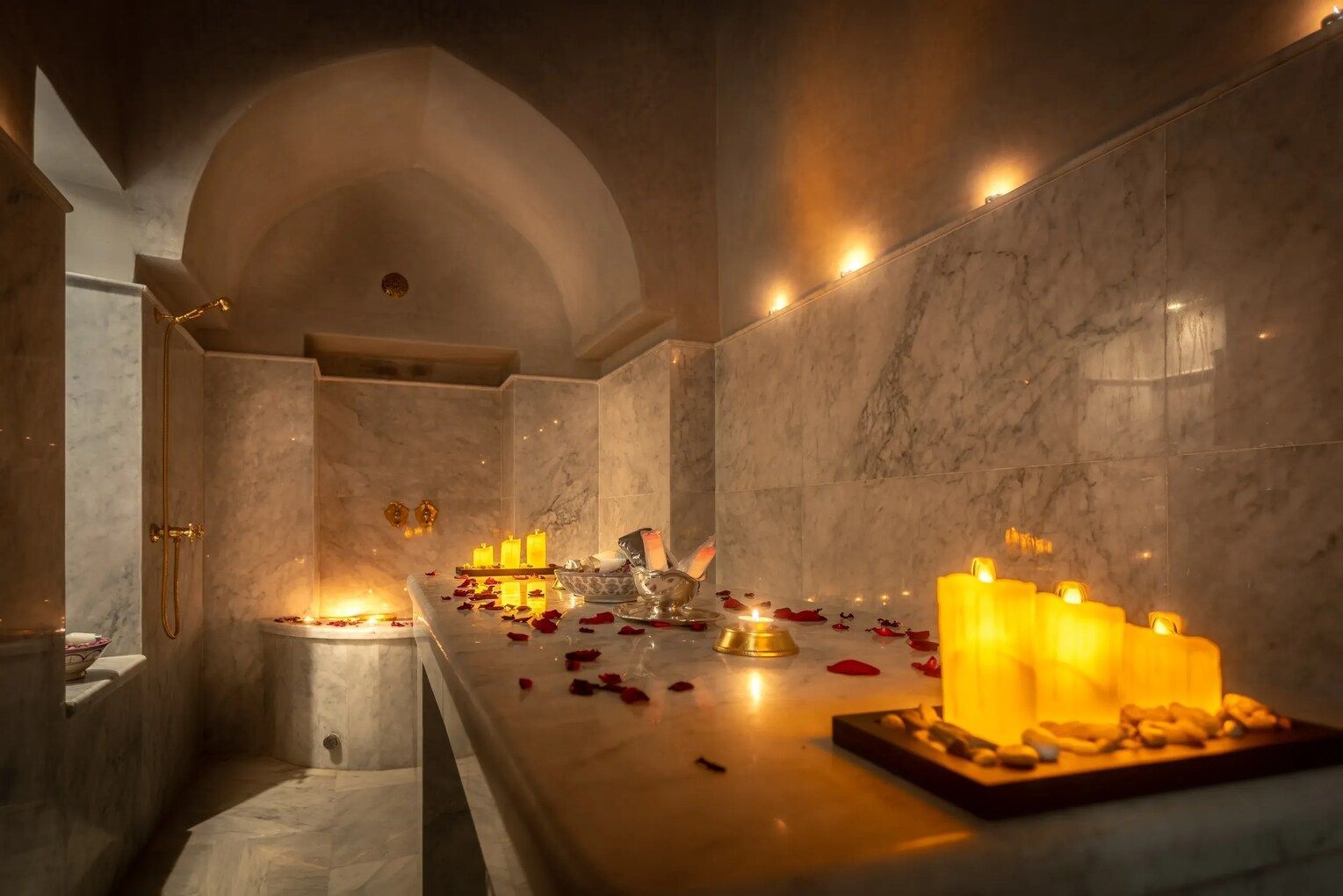 Marble hammam with lit candles and rose petals, creating a relaxing ambiance.