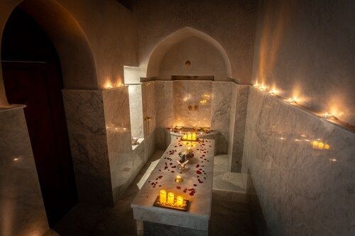 Spa room with candles and massage table. Dimly lit, white walls and arched doorway.