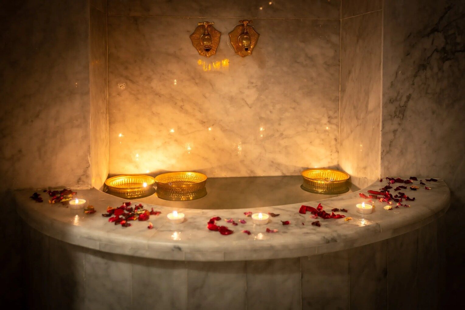 Marble spa alcove with candles, golden bowls, and rose petals, creating a relaxing ambiance.