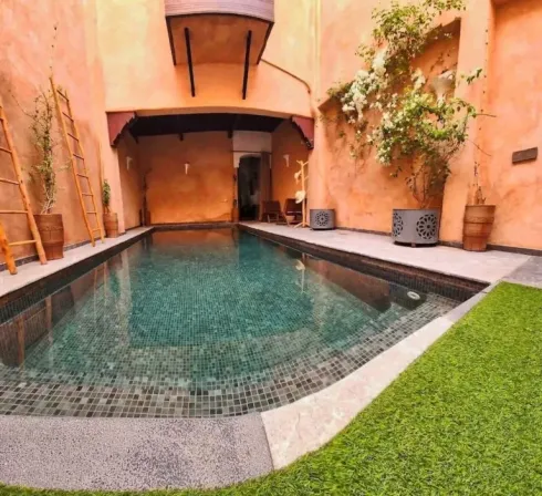 Indoor pool with teal water in courtyard; peach walls, greenery, and steps leading into the pool.