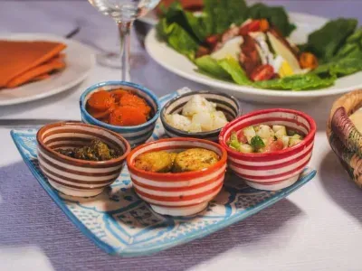 Colorful bowls of appetizers on a patterned tray, with salad in the background, set on a white tablecloth.
