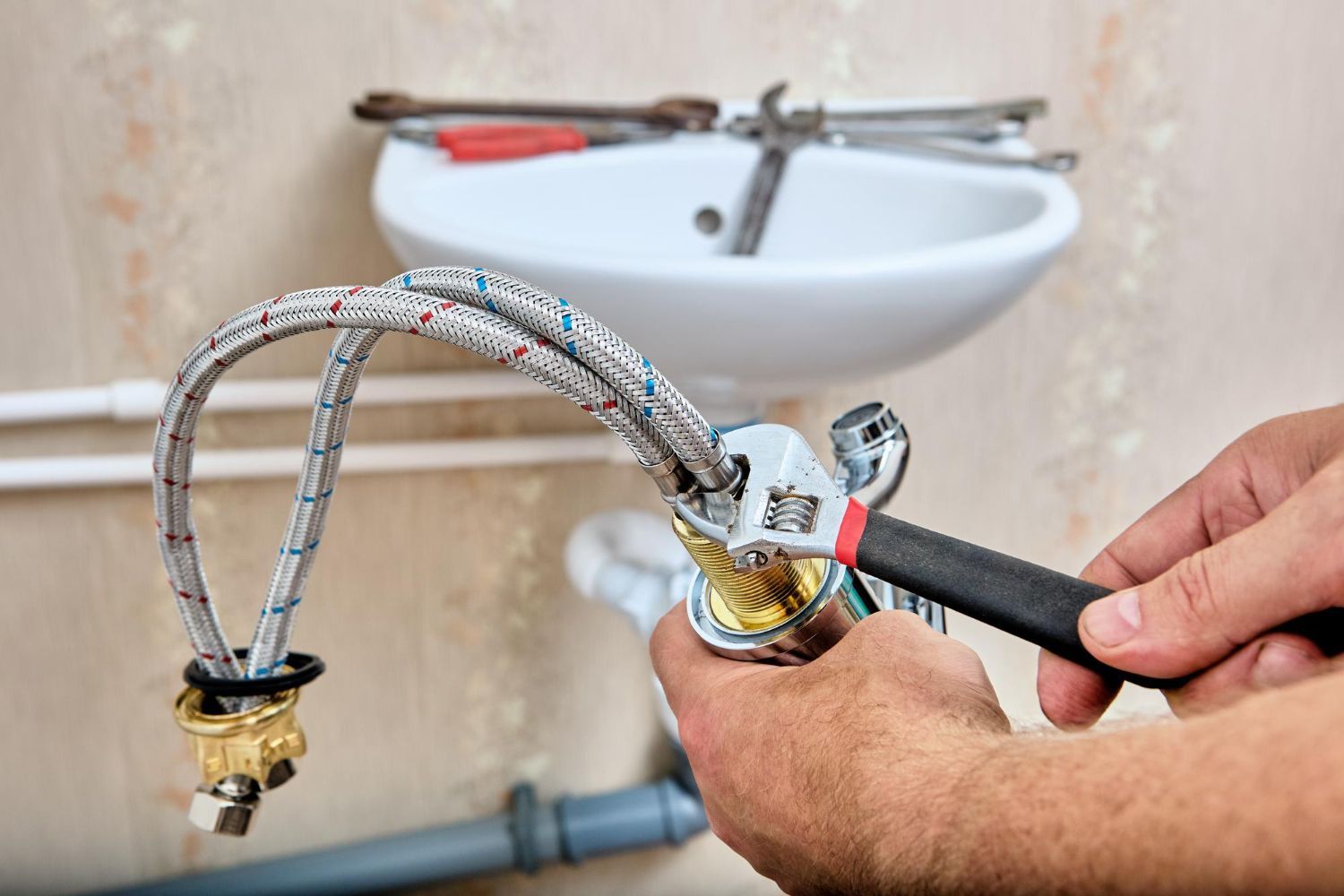 Hands of a person using a wrench to connect a water hose to a faucet under a sink.