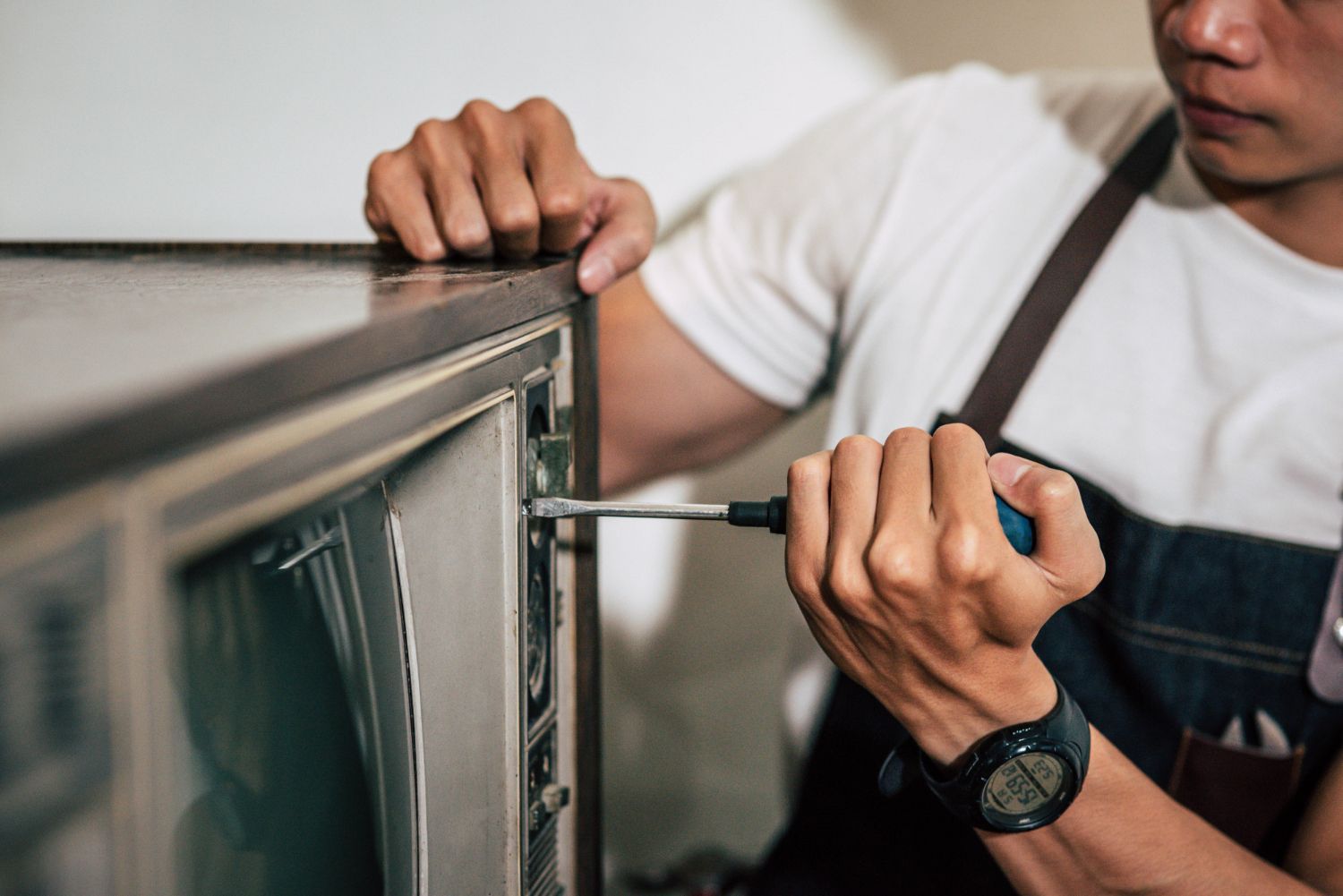Person using a screwdriver to repair a vintage television.
