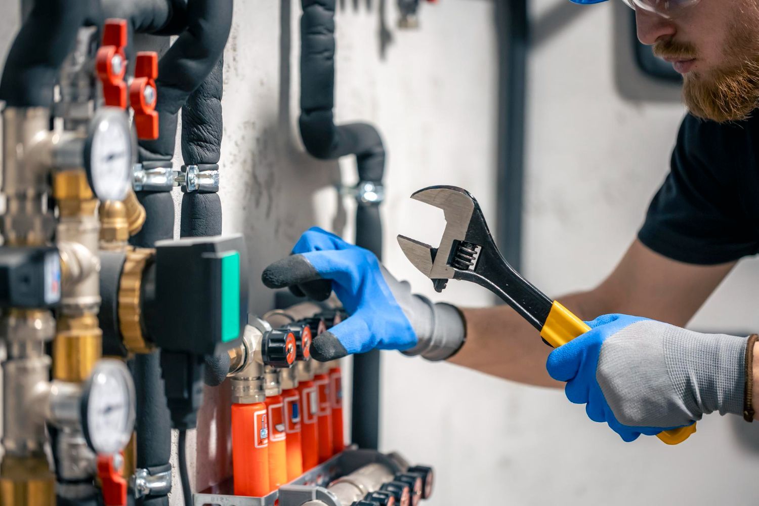 Plumber in blue gloves, using a wrench on pipes and valves.