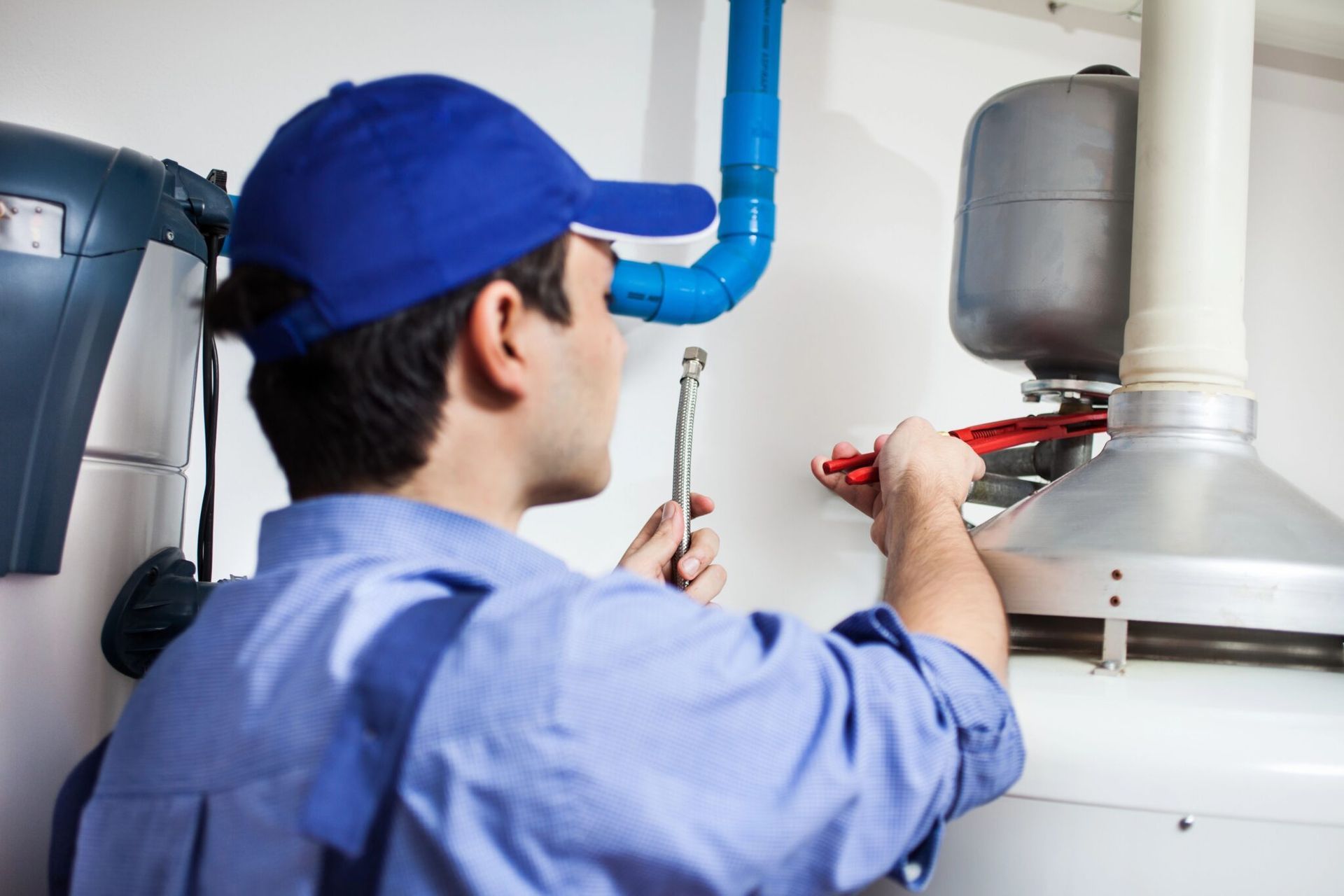 Plumber in blue uniform uses a wrench on a water heater and pipes in a utility room.