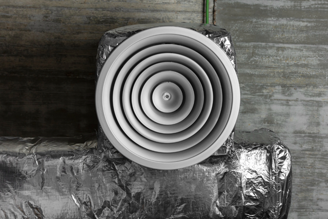 Ceiling vent with concentric rings, attached to insulated ductwork against a concrete wall.