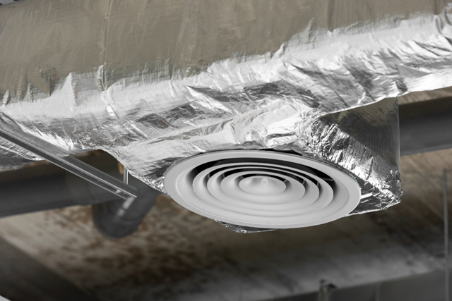 Air vent with silver metallic insulation on ductwork in a building.
