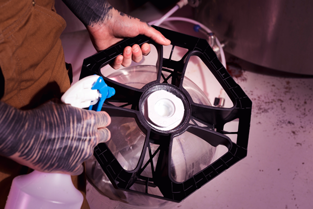 Person spraying a black octagonal filter, likely for a brewing process, with a blue spray bottle.