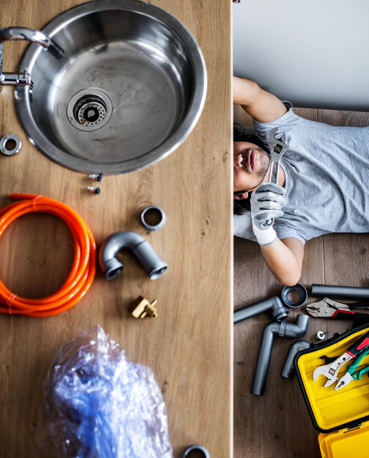 Plumber working on a sink, tools and parts on a wooden surface.