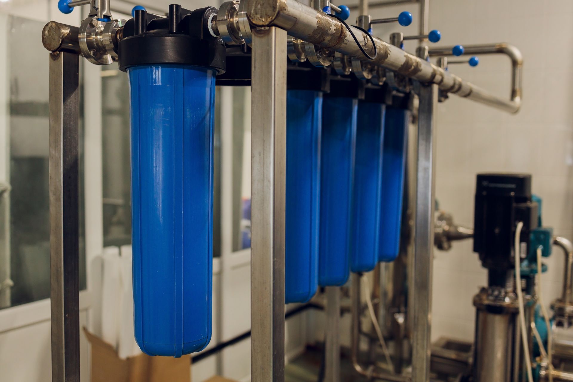 Blue water filter housings in an industrial setting, attached to metal pipes.