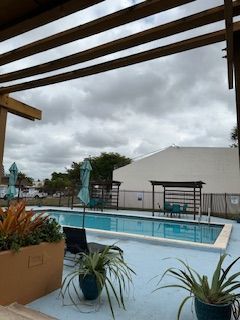 a large swimming pool surrounded by potted plants and umbrellas on a cloudy day