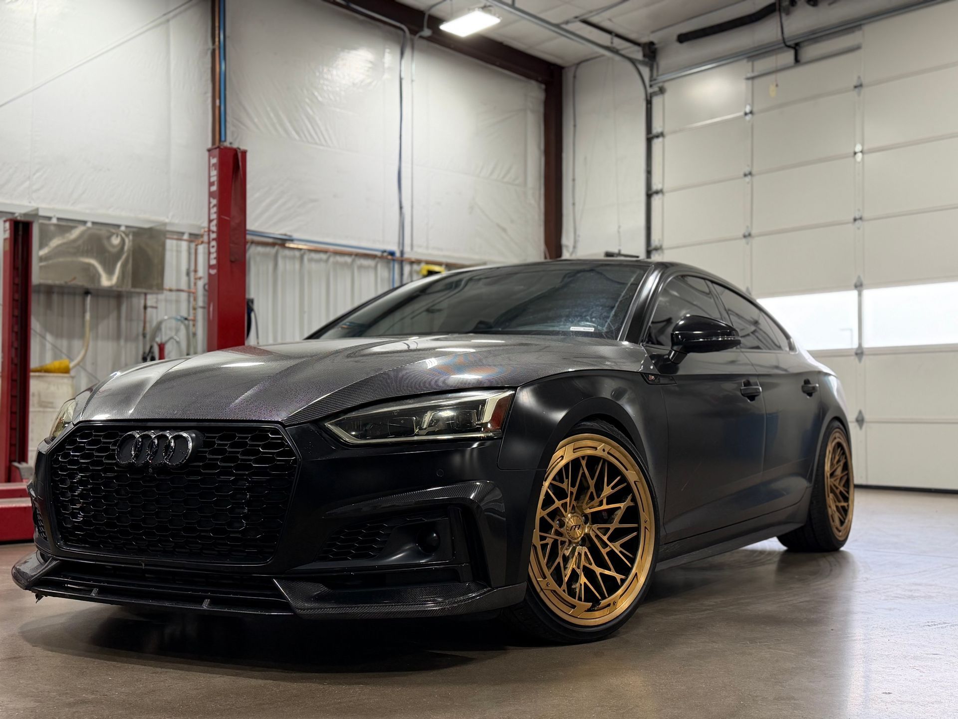 Black modified sedan with gold rims parked in a garage