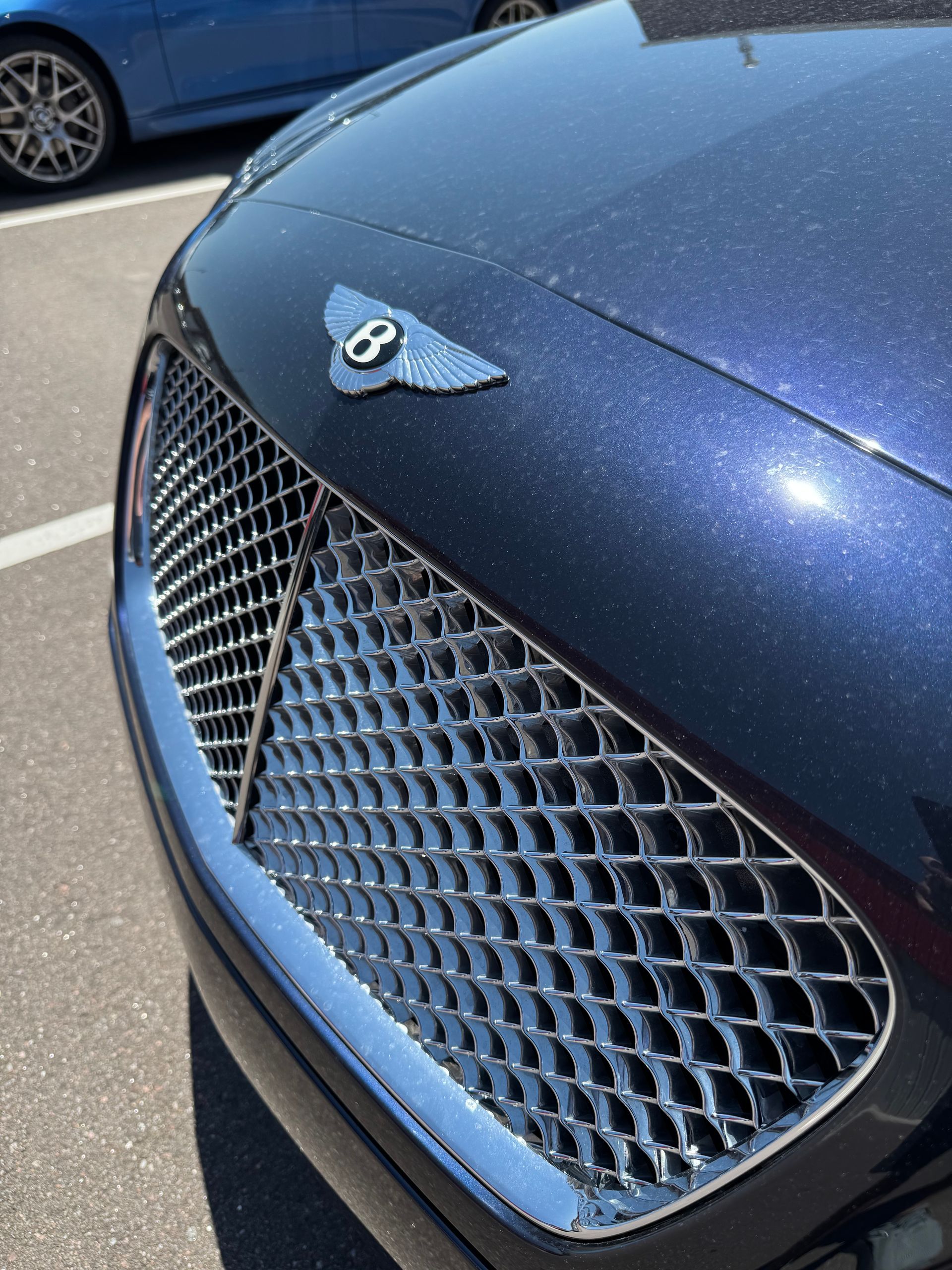 Close-up of a dark blue Bentley car's front grille and hood | Peak European