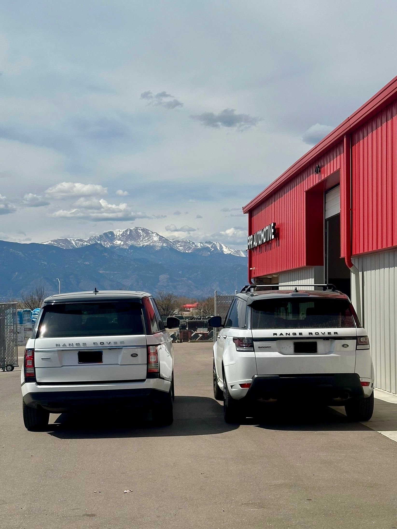 Two white SUVs parked beside a red building with mountains in the background.