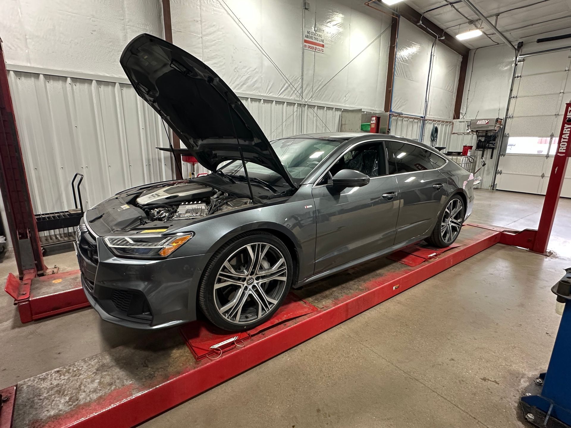 Gray sedan on a lift in an auto repair shop with its hood open.