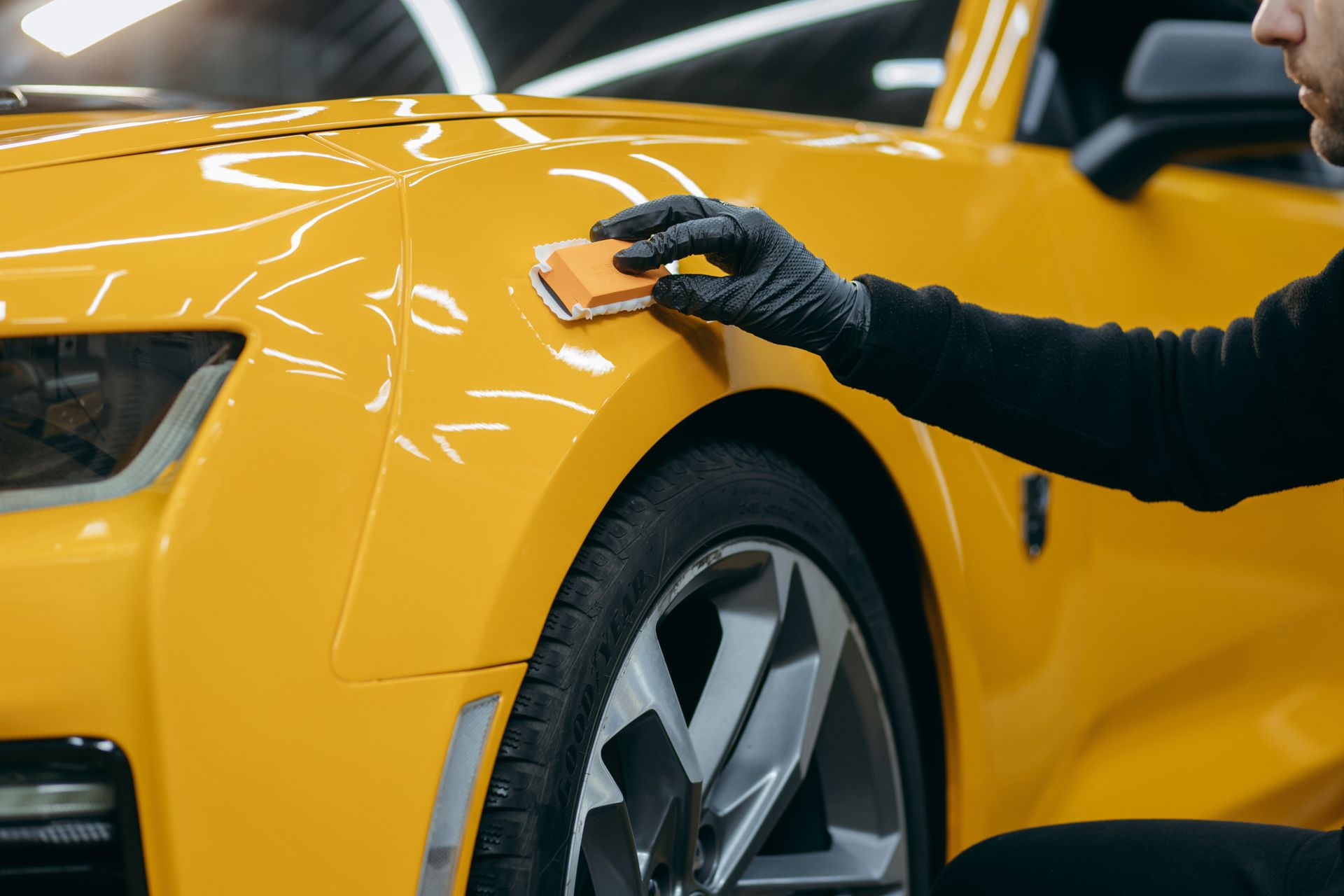 Person in black gloves applying ceramic coating to a bright yellow car.