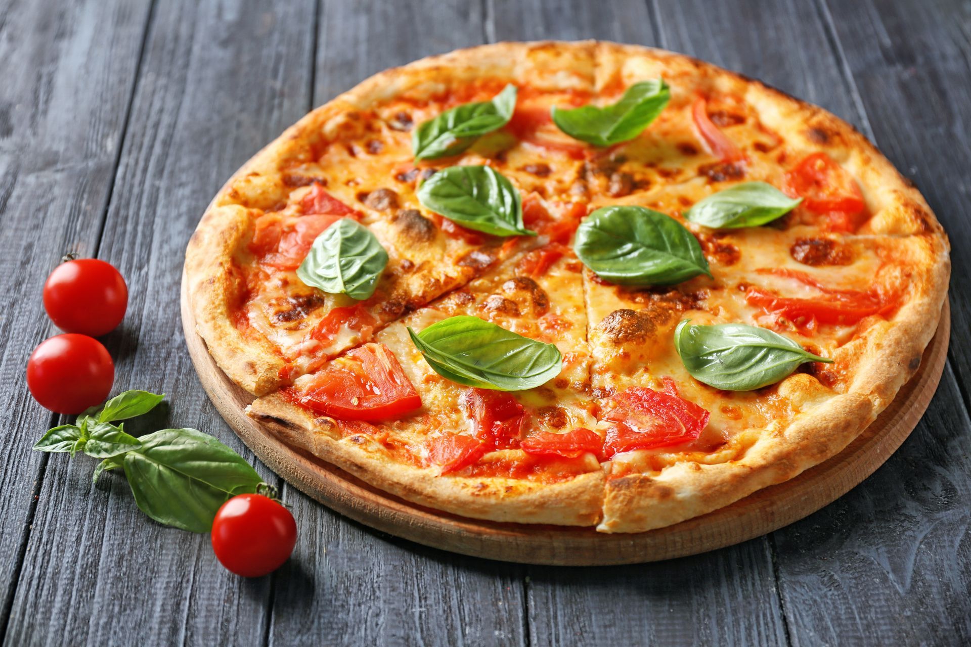 Pizza topped with tomatoes and basil on a wooden board with cherry tomatoes next to it. Pizza topped with tomatoes and basil on a wooden board with cherry tomatoes next to it.