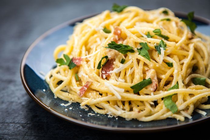 Spaghetti carbonara with bacon, Parmesan, and parsley on a blue plate.
