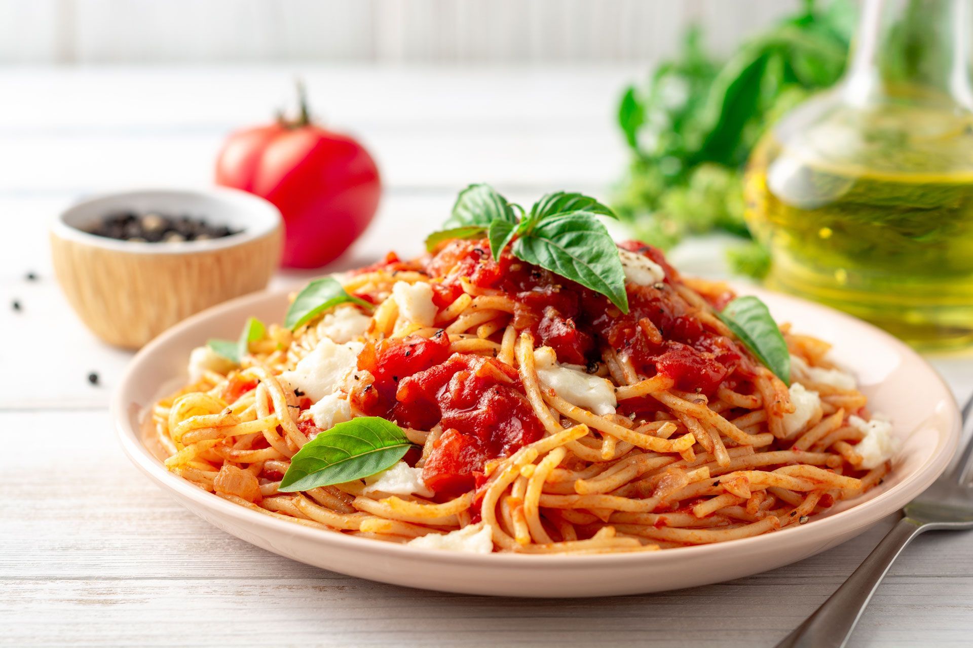Spaghetti with tomato sauce, basil, and cheese on a pink plate, with ingredients in the background.