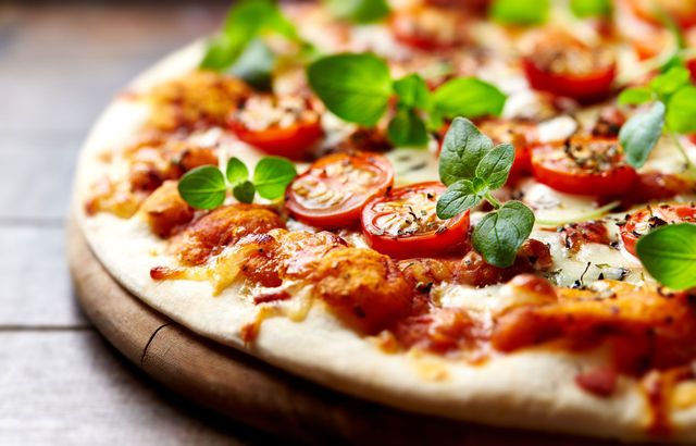 Pizza with tomatoes, herbs, and cheese on a wooden board.
