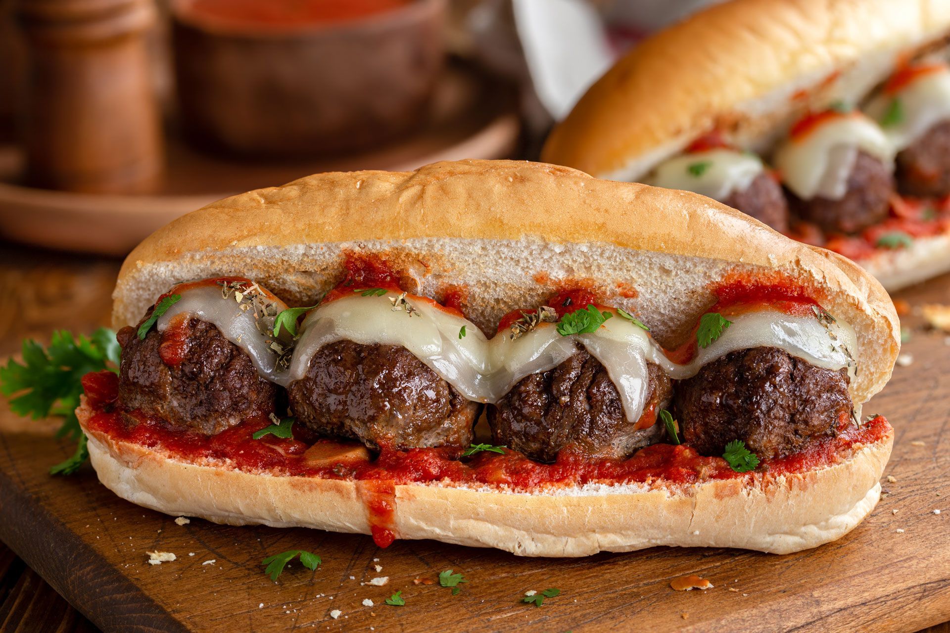 Meatball sub with melted cheese and marinara sauce on a wooden board.