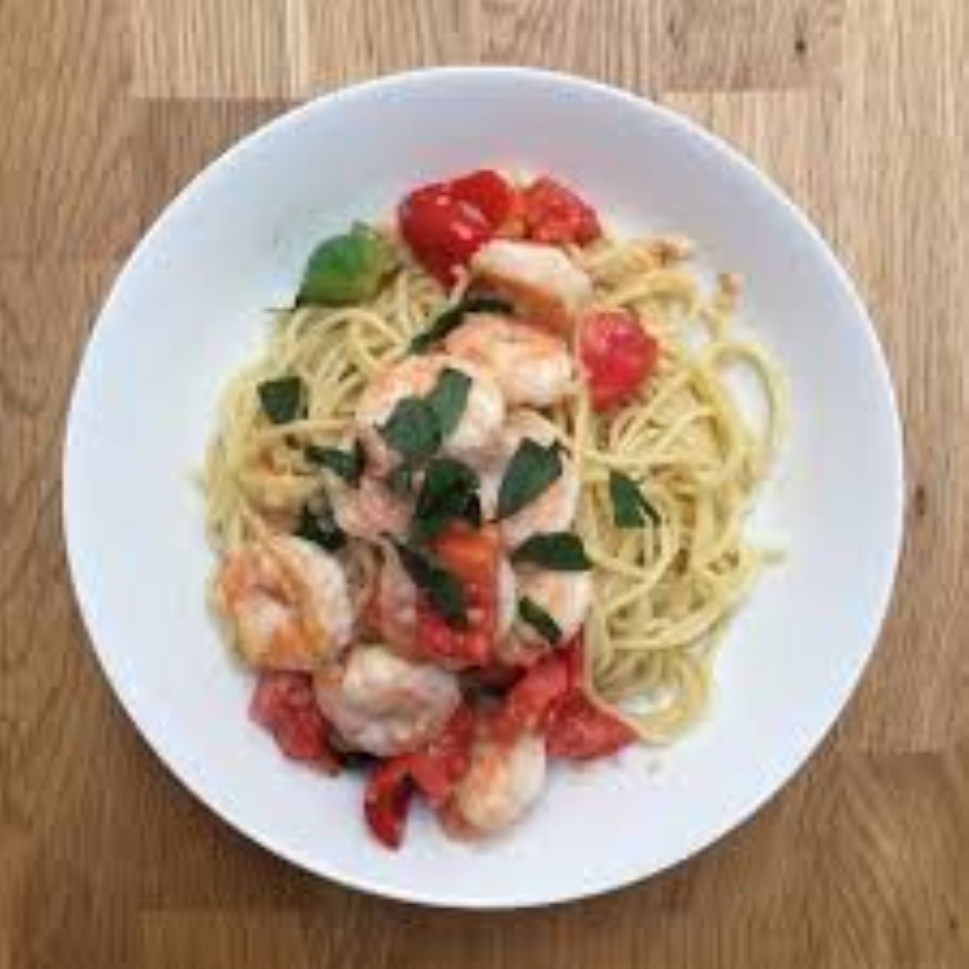 Spaghetti dish with shrimp, tomatoes, and basil on a white plate.