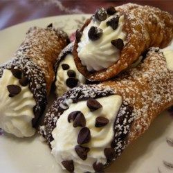 Cannoli pastries with creamy filling, chocolate chips, and powdered sugar on a plate.