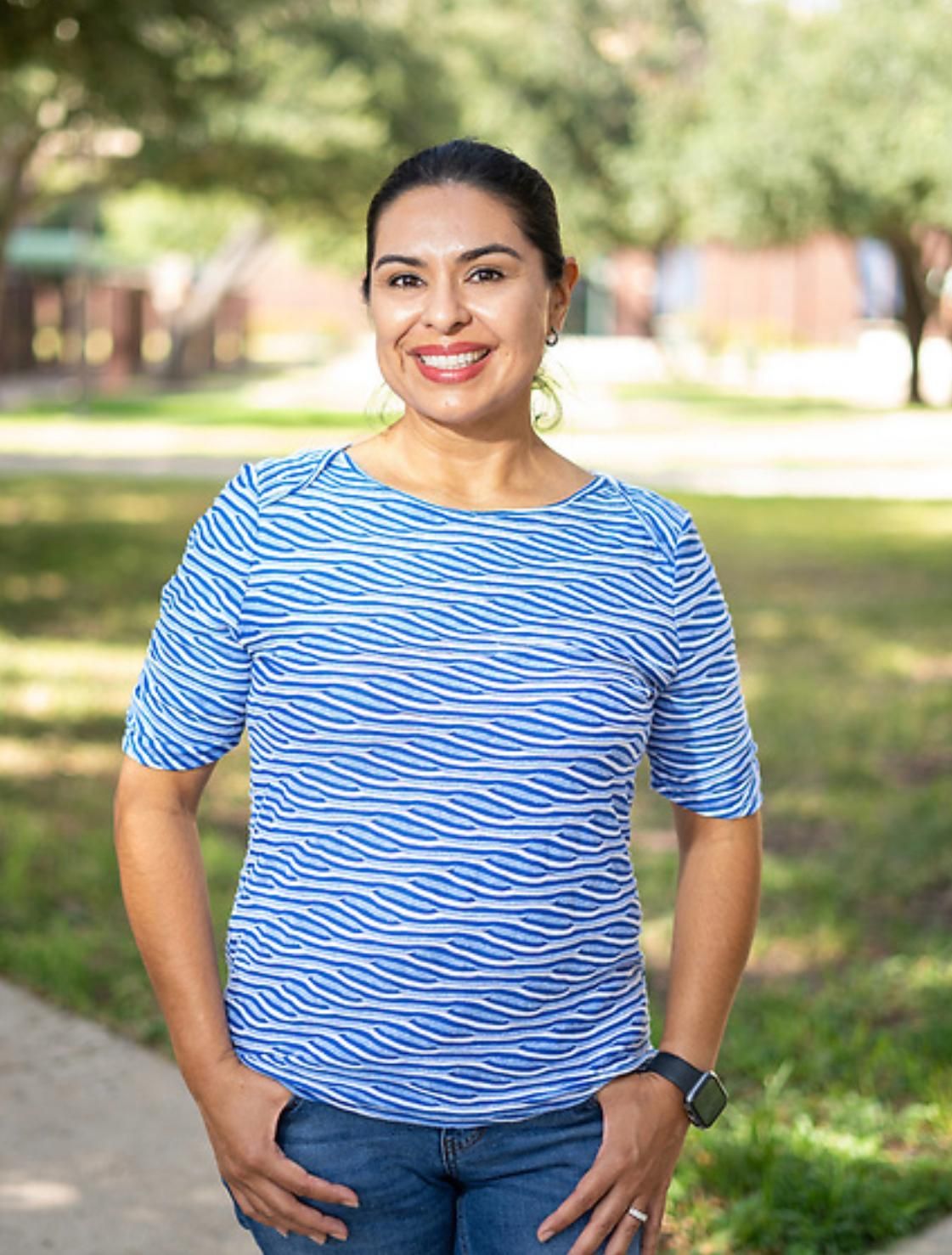 a woman in a blue shirt is smiling in front of a palm tree .