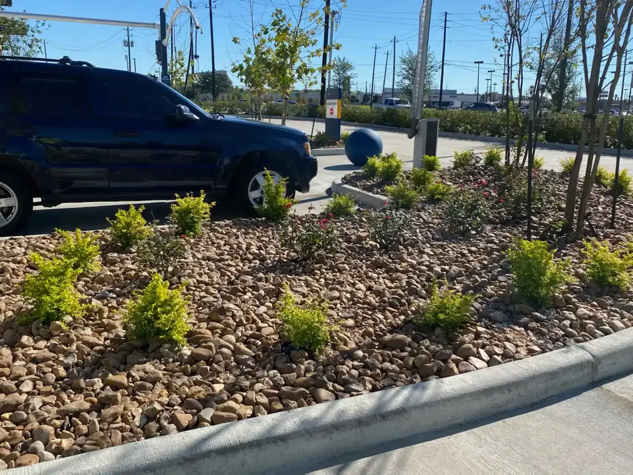 A black suv is parked in a parking lot surrounded by rocks and plants.