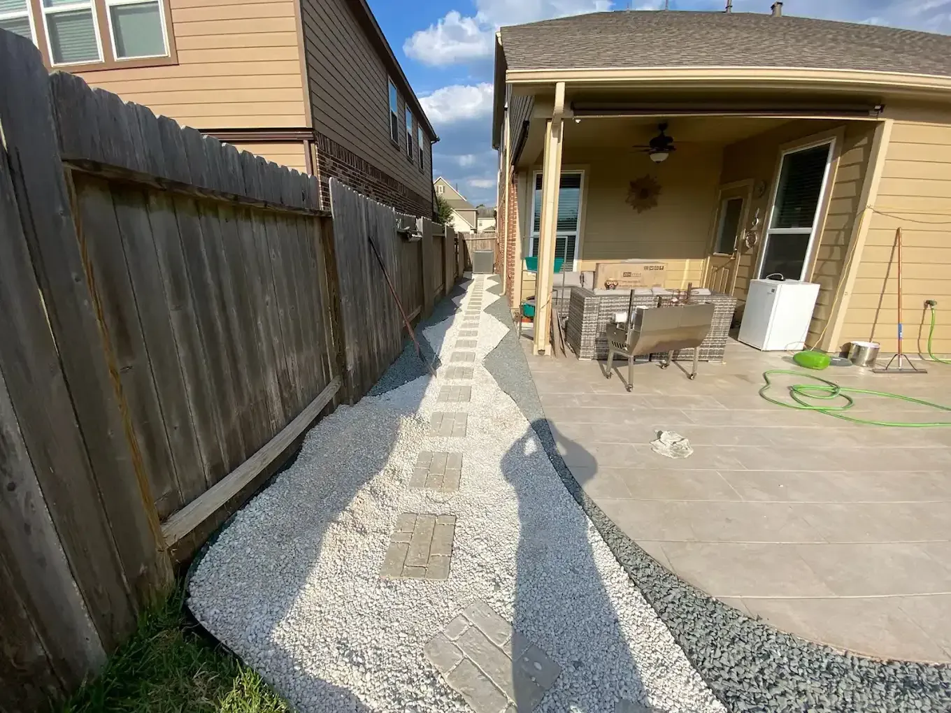 A walkway leading to a patio with a wooden fence and gravel.