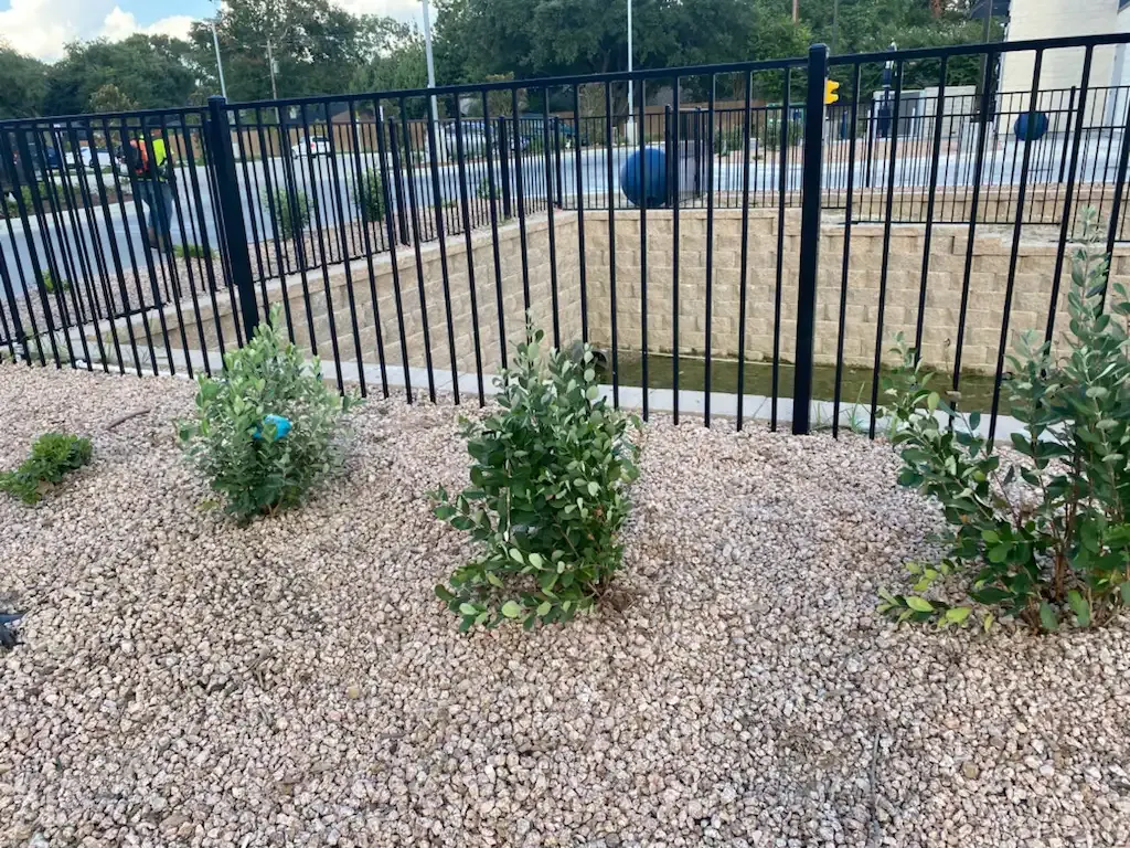 A black metal fence is surrounded by gravel and plants.