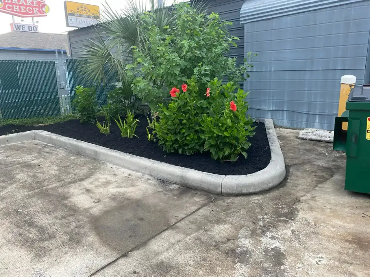 A concrete curb with a bush and flowers in front of a building.
