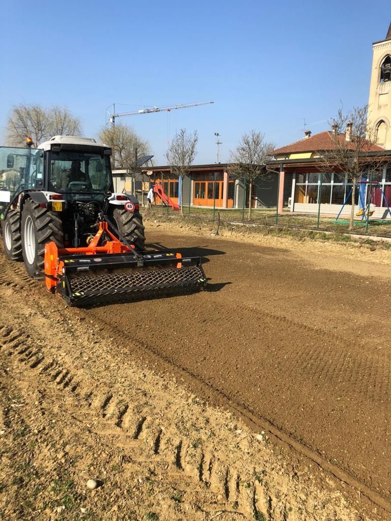 Trattore che livella un campo di terra battuta accanto agli edifici in una giornata di sole
