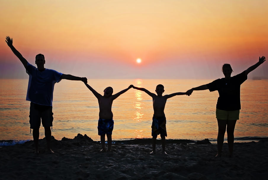 Family silhouetted on a beach holding hands at sunset
