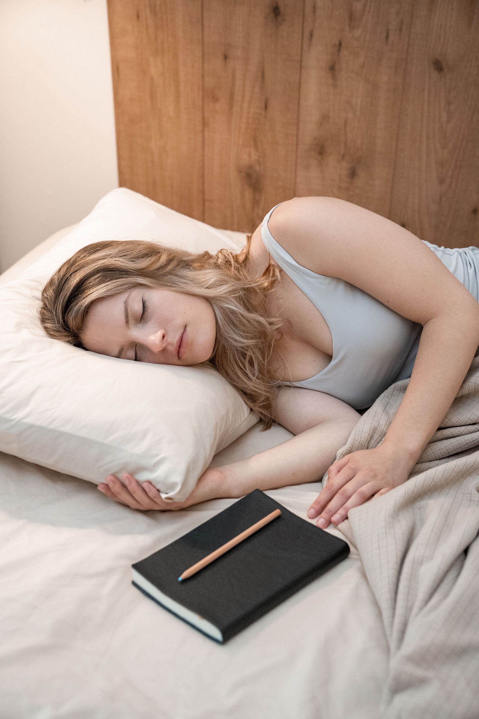 Woman sleeping in bed beside a notebook and pencil on a beige blanket