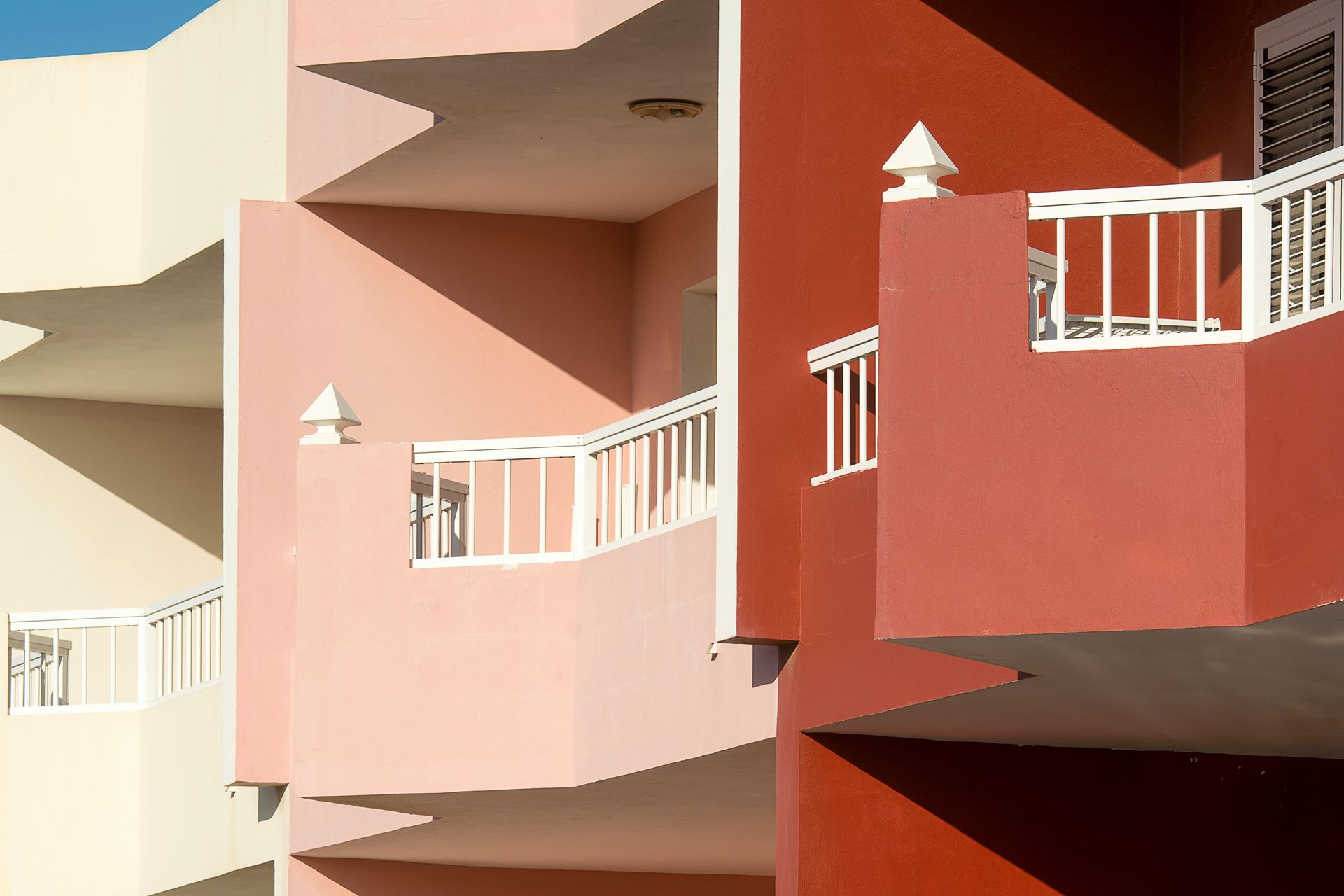 Abstract view of pastel and red apartment balconies with white railings and angular shadows