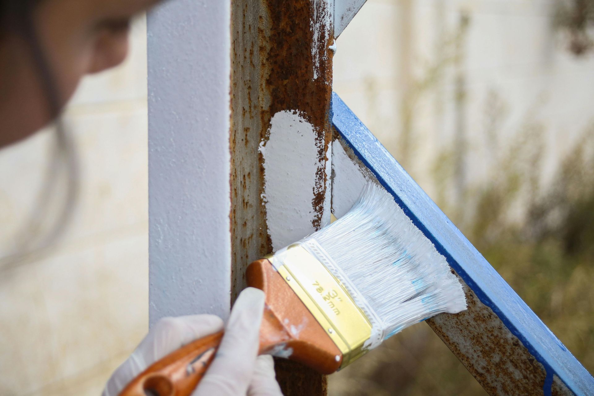 Gloved hand painting a rusty metal window frame white with a brush.