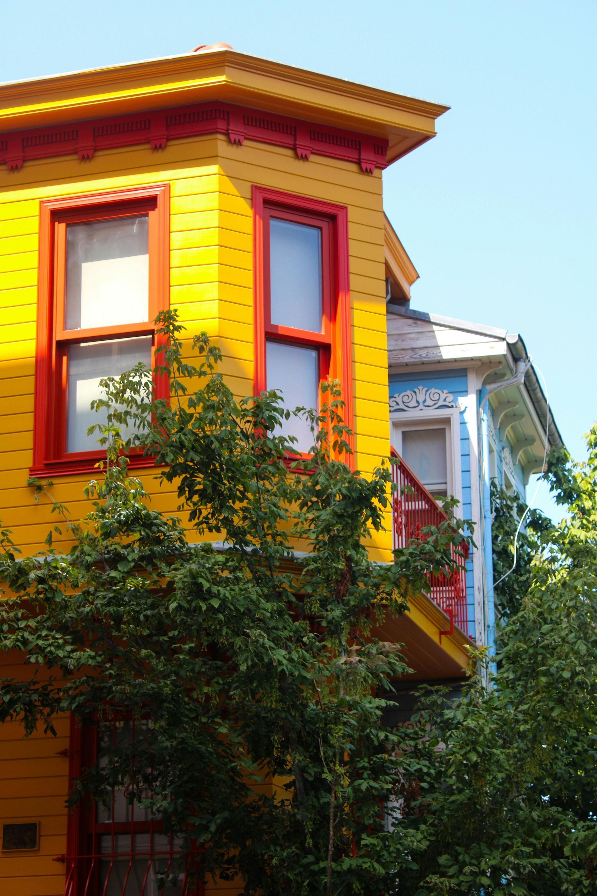 Bright yellow and red house facade with a bay window, partly covered by green trees