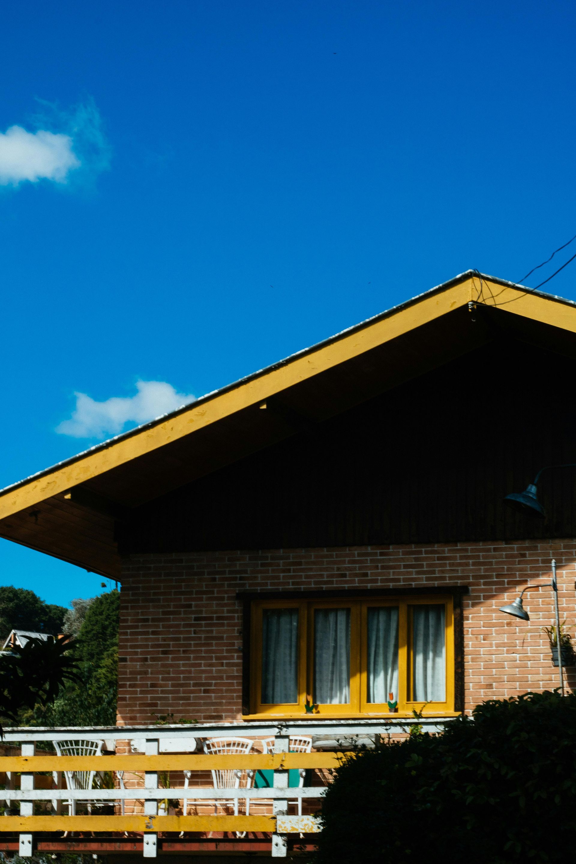 Brick house with a steep yellow-trim roof under a bright blue sky, with a white railing in front