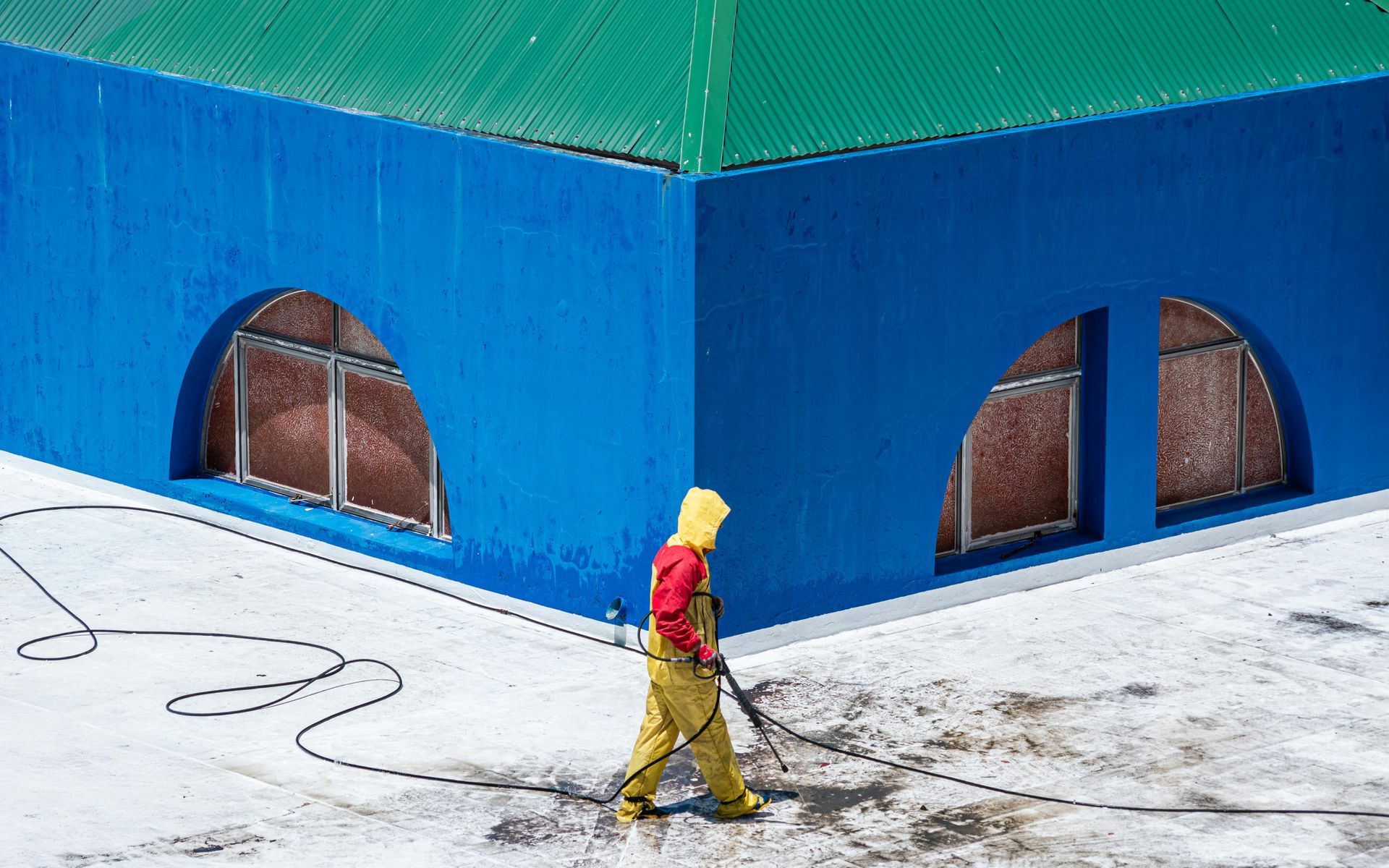 Person in yellow jacket walks past a blue building with arched windows on a snowy sidewalk.