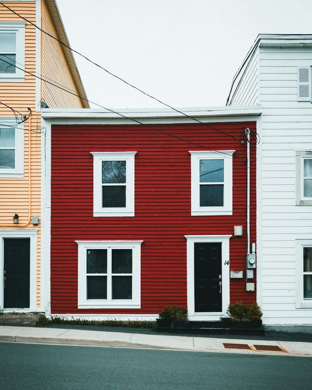 Red house with white trim and two windows beside white buildings on a street.