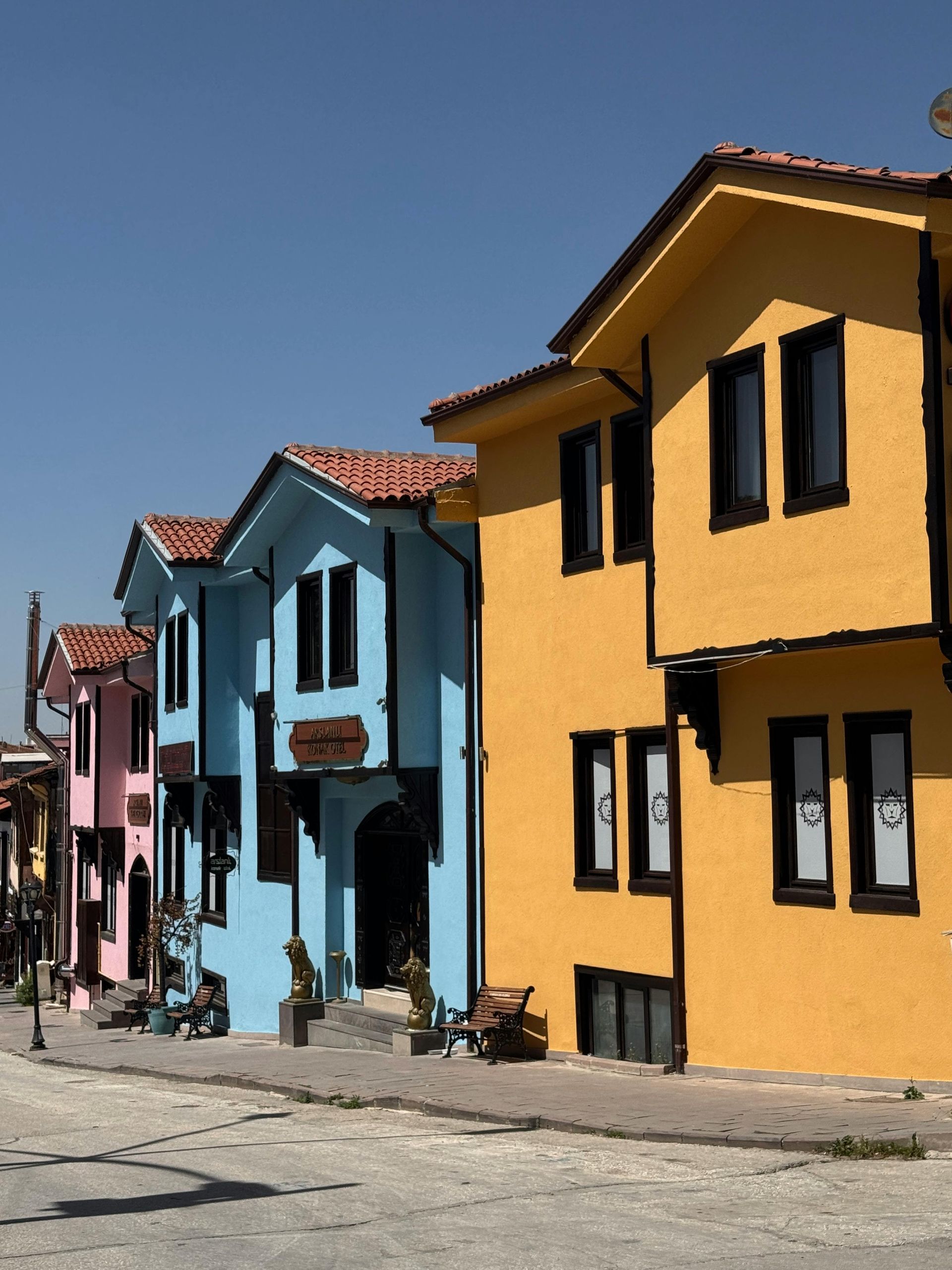 Colorful row of houses on a sunny street, including blue, yellow, and pink facades with tiled roofs.