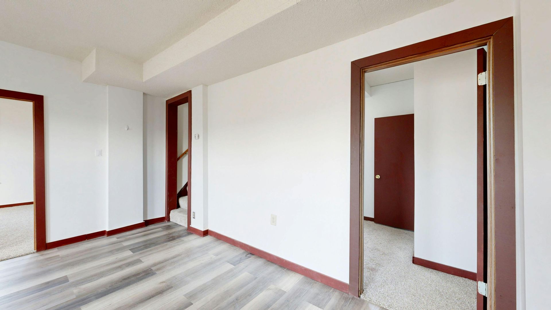Empty modern room with light walls, gray flooring, and dark wood-trimmed doorways