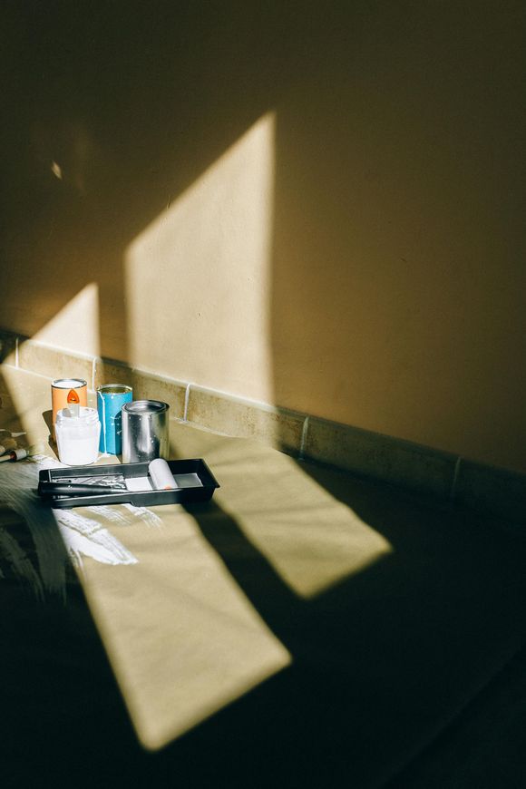Cans and a tray on the floor in sunlight, with sharp window shadows on a wall and floor
